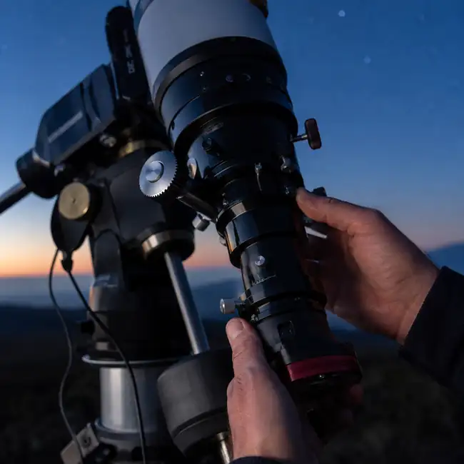 Hands adjusting a telescope at twilight on Hawaiʻi Island