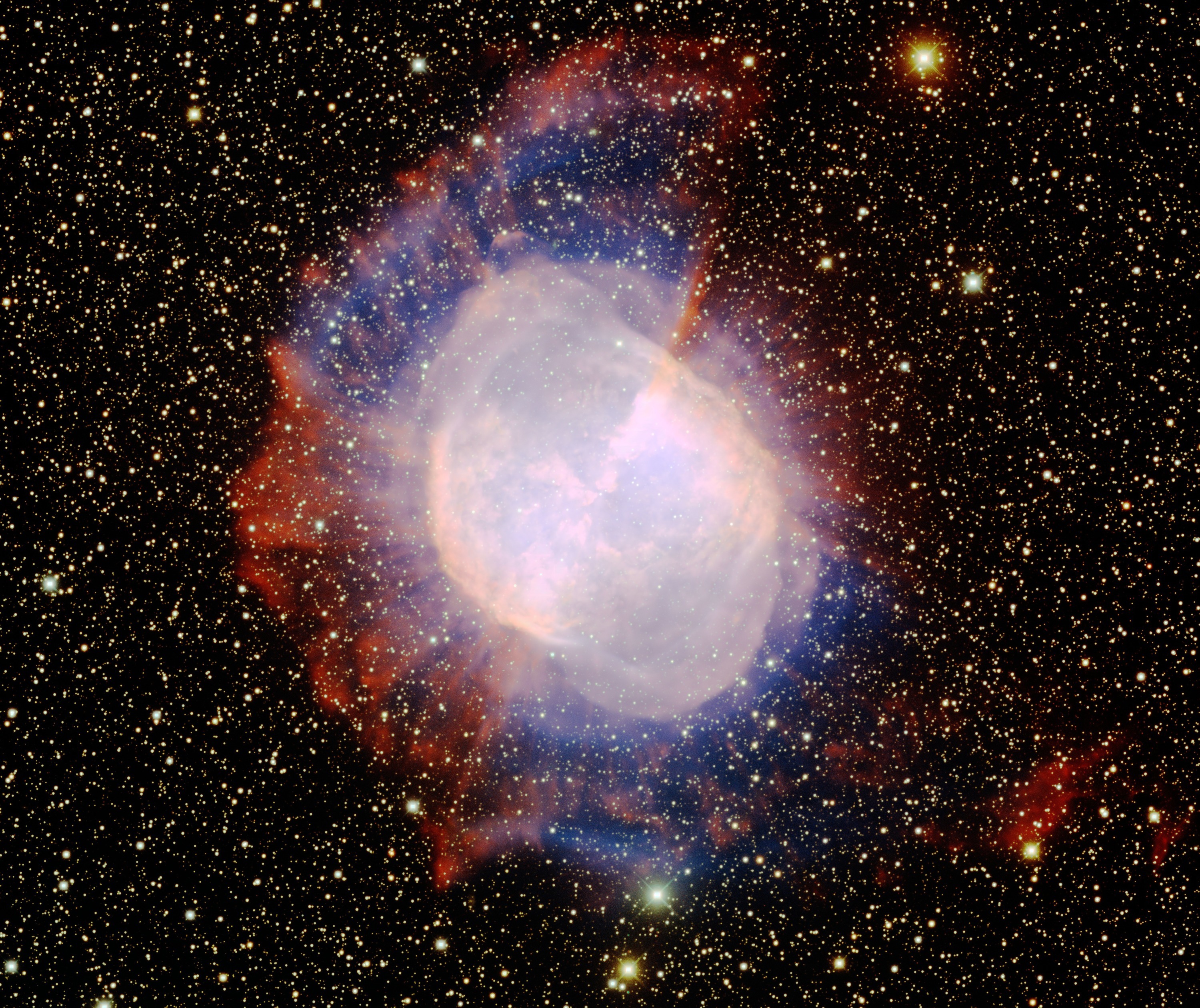 Deep Mayall telescope photograph of M27: two luminous lobes, a hot central star and faint ragged outer gas, surrounded by a rich star field.